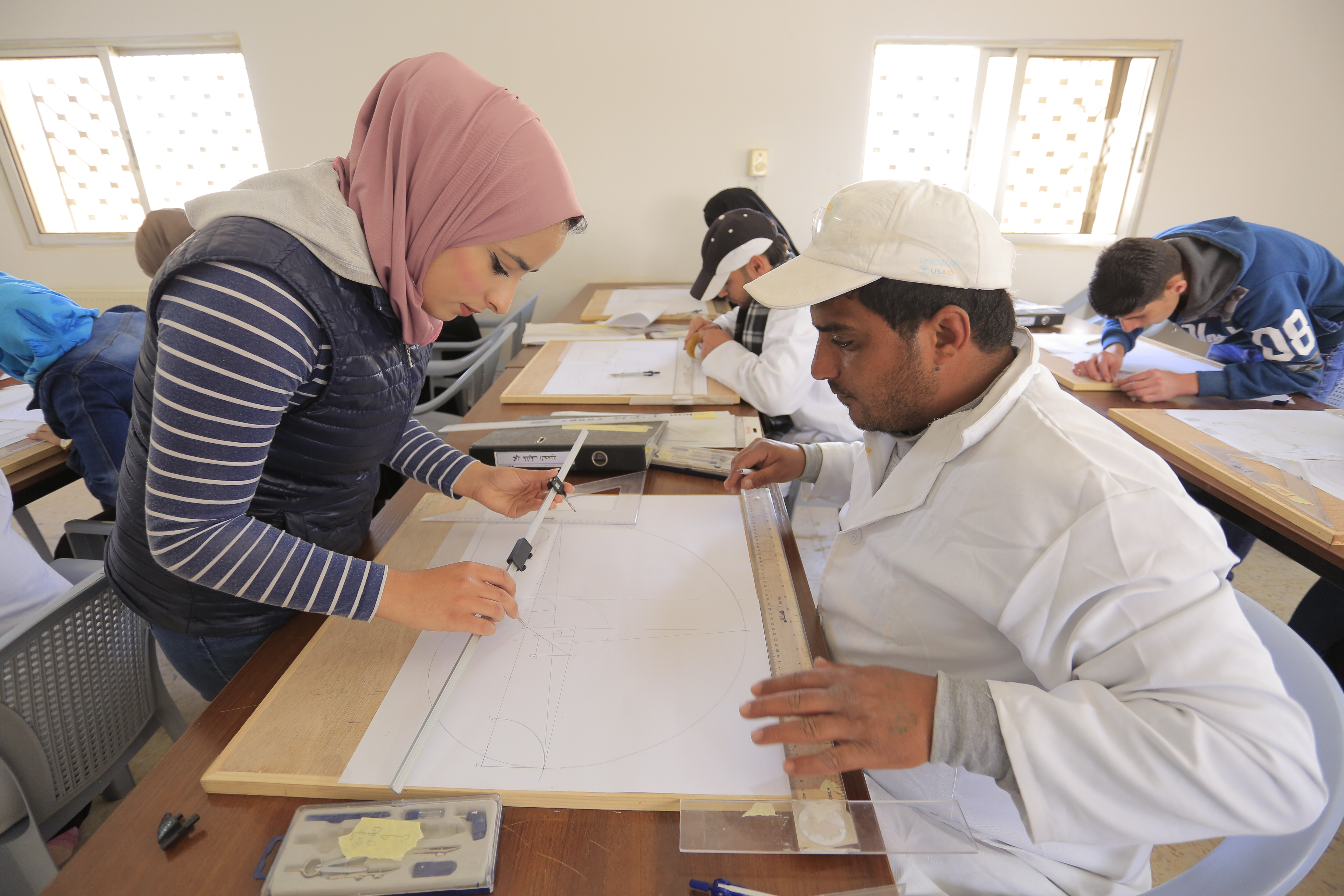 Nour Shdaifat, a leader of WMF’s stonemasonry training program, instructs Hasan, a Syrian trainee, on technical drawings