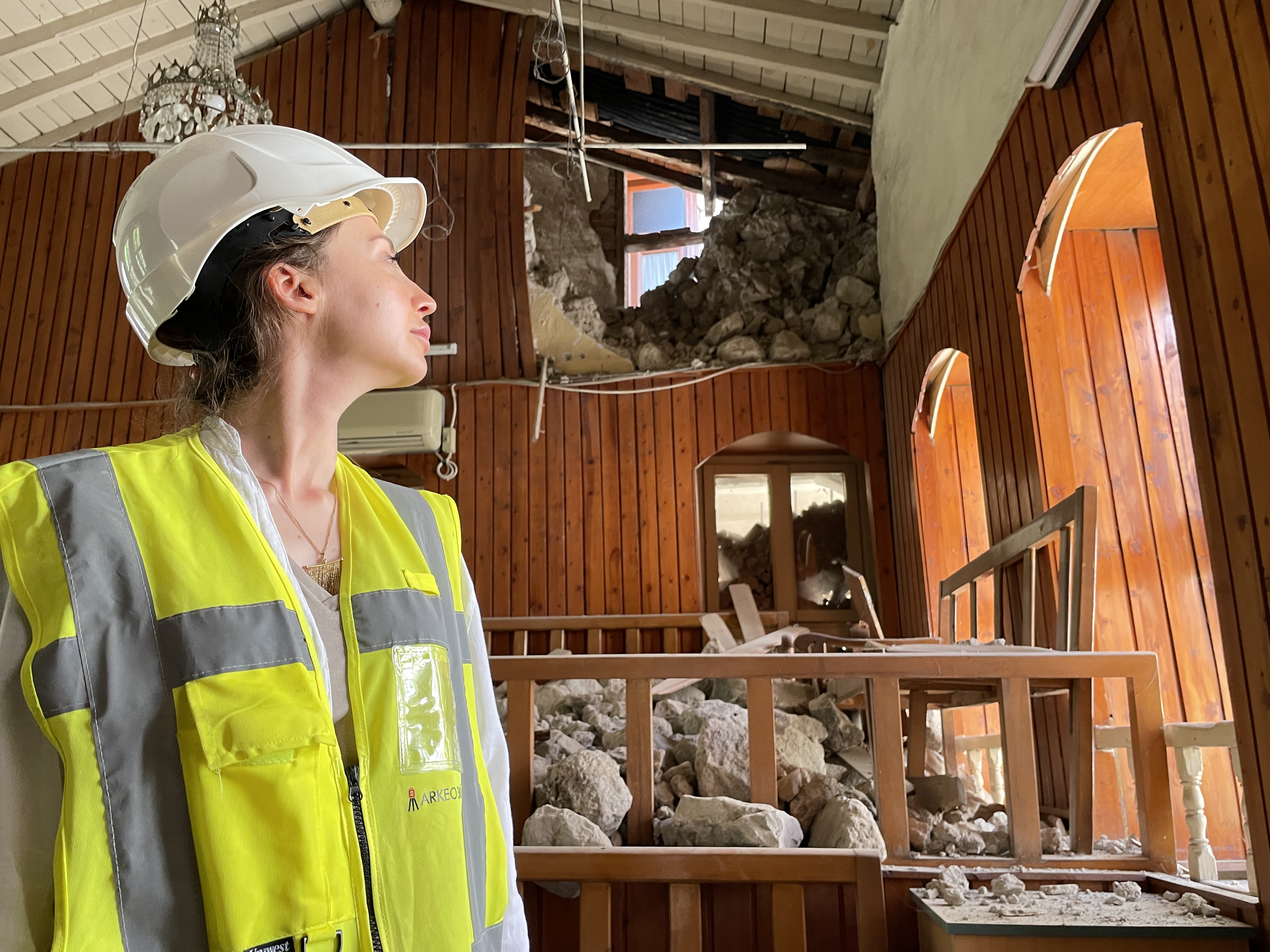 Profile view of woman in safety helmet and hi-vis vest inside an earthquake-damaged building