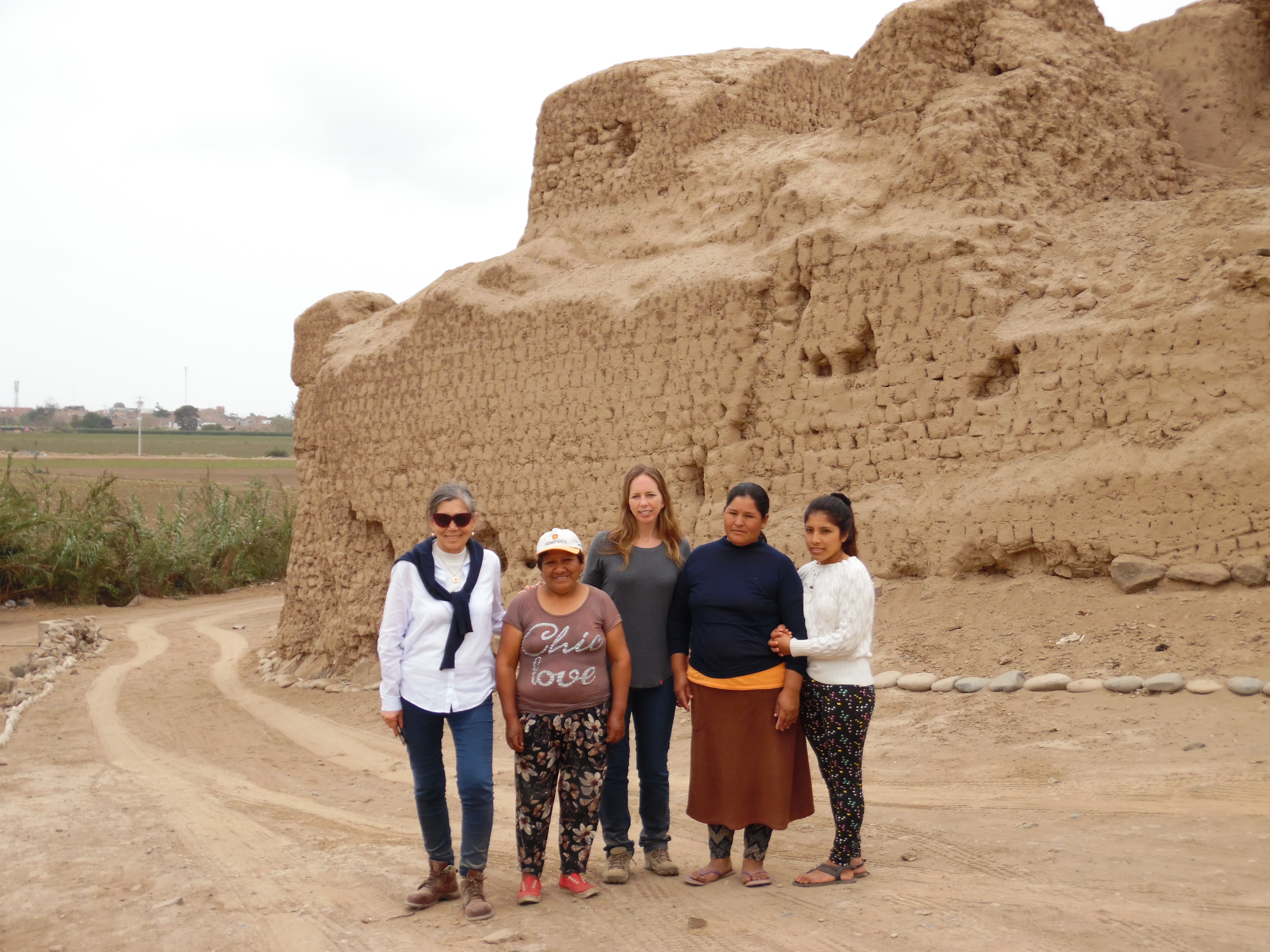 Martha Zegarra (Executive Director, WMF Peru), Francesca Fernandini (Archaeological Program Director, Cerro de Oro), and a group of local women stand in front of the wall that surrounds the site.
