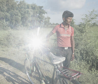 Straight-on view of a man in a red shirt looking away from the camera and holding a bike that catches the sunlight strongly