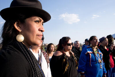 Close-up of a woman with a black hat staring into the distance as she stands with a group of other Indigenous women