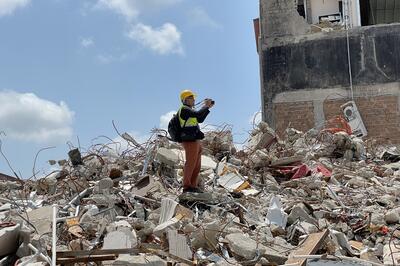 Man in safety gear standing on huge hill of rubble, looking off to the side