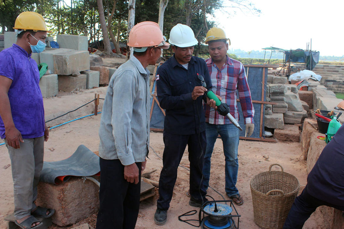 Phnom Bakheng site manager Mou Var, shown here in a blue uniform and white hard hat, explains to EFEO staff how to set the welding machine, 2017