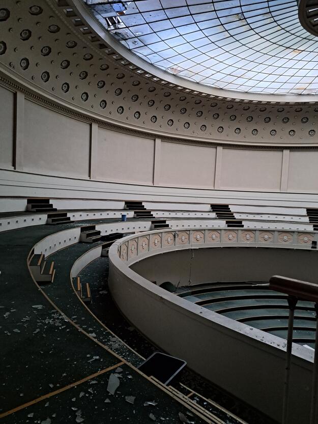 Round seating area topped by glass dome with several panels broken and glass on floor.