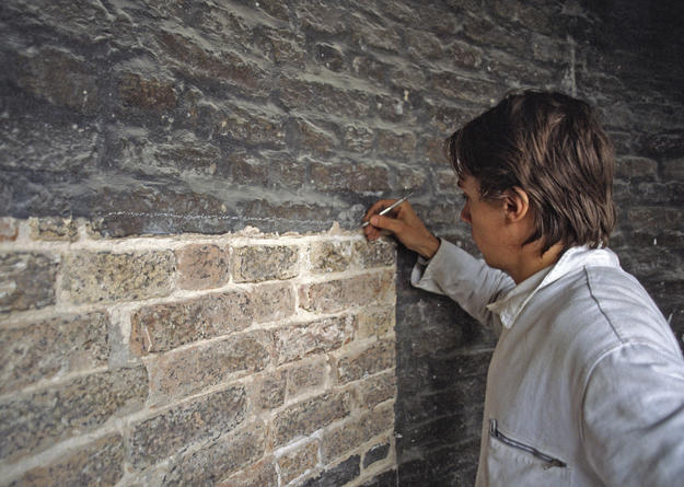 A conservator removes the destructive stuccatura from the structure's bricks, 1981