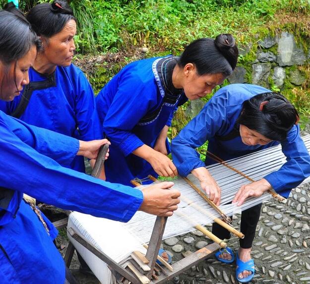 Group of women in indigo clothing around a loom