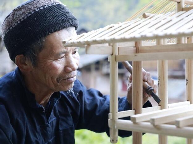 Man in wool cap using blade to refine wooden model of a house