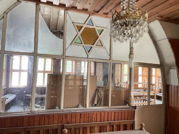 Brown wood interior with shattered windows and stained glass in the shape of the star of David.