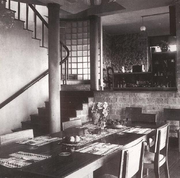 Black-and-white photo of dining room table with curved staircase in background.